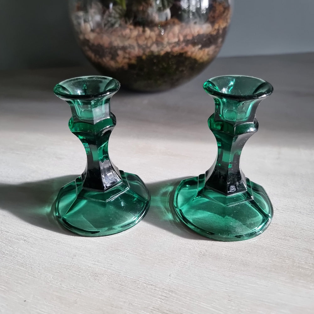 Pair of vintage emerald green glass candlestick holders catching light on a tabletop.