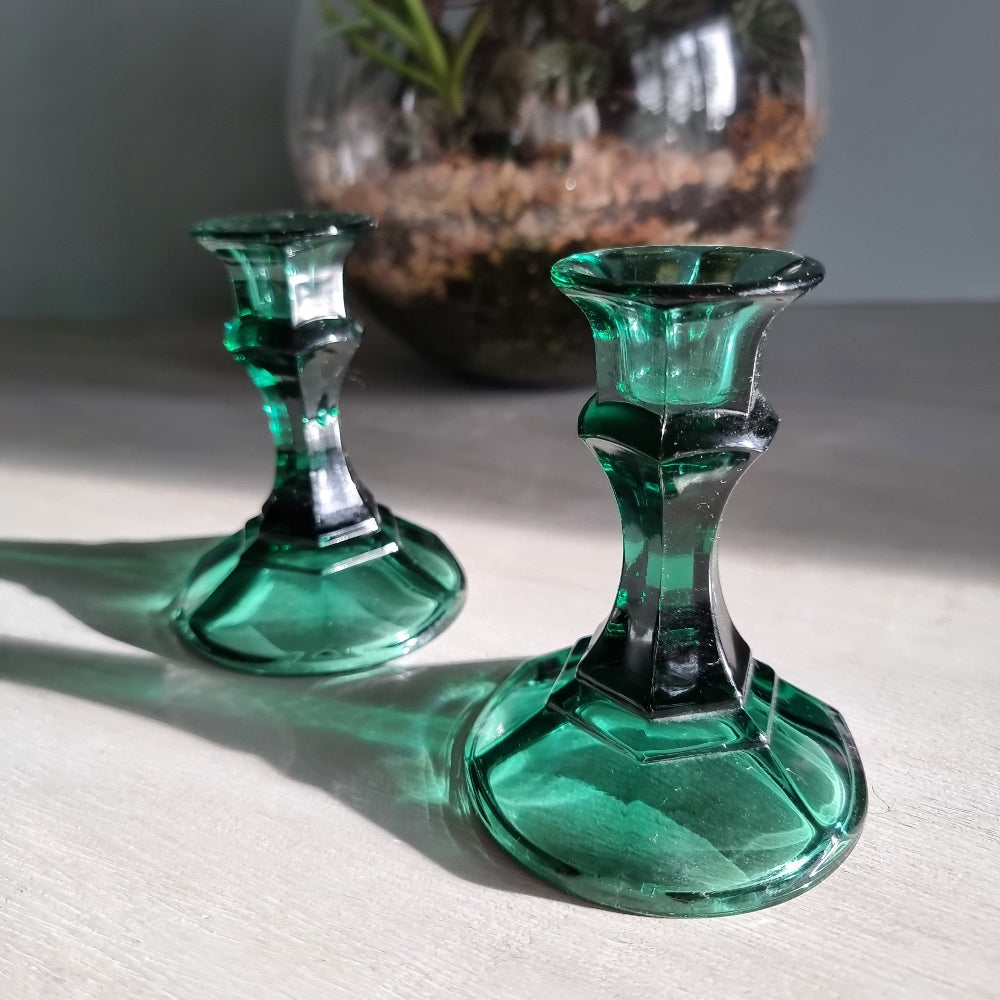 Pair of vintage emerald green glass candlestick holders catching light on a tabletop.