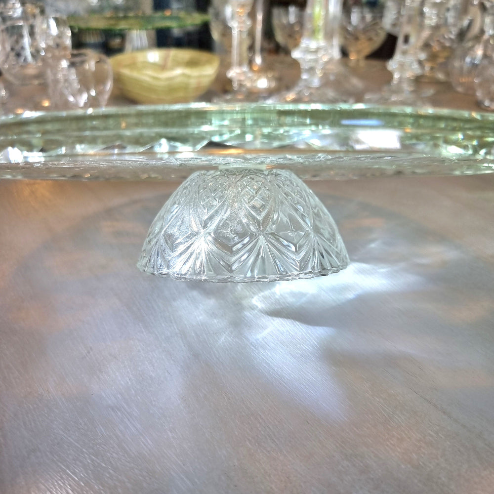 Clear pressed glass cake stand with starburst pattern and raised foot, catching light on a tabletop.