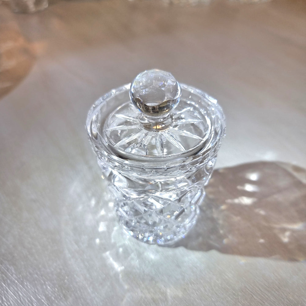 Small crystal jam jar with cut-glass lattice pattern and round lid knob catching the light.