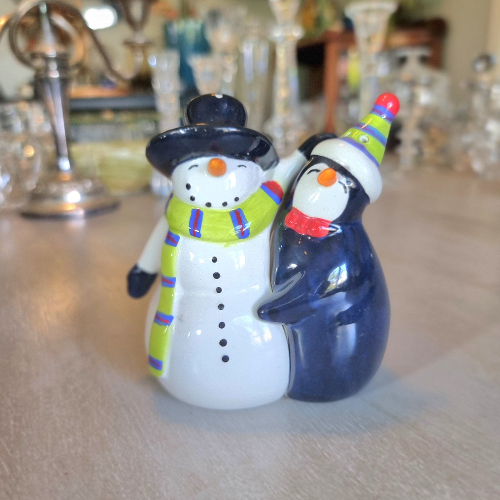 Ceramic salt and pepper shakers shaped as a hugging snowman and penguin.