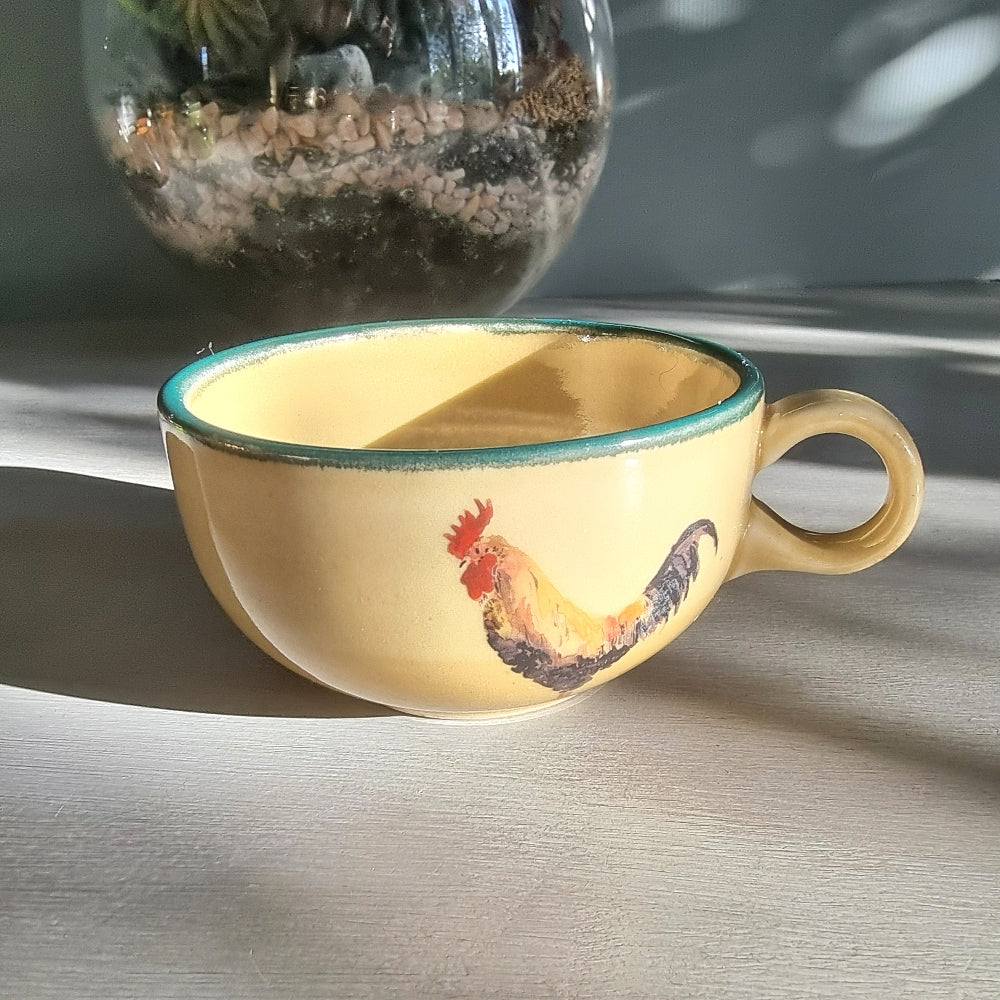 Ceramic rooster mug and cup set in warm yellow tones, styled on a tabletop in natural light.