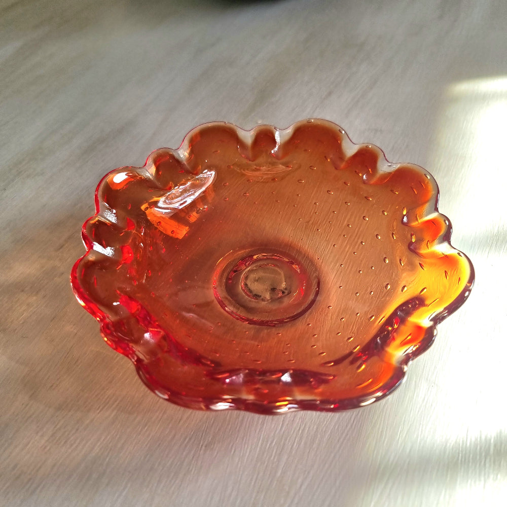 Amber art glass dish with ruffled edge and bubble detail catching warm sunlight