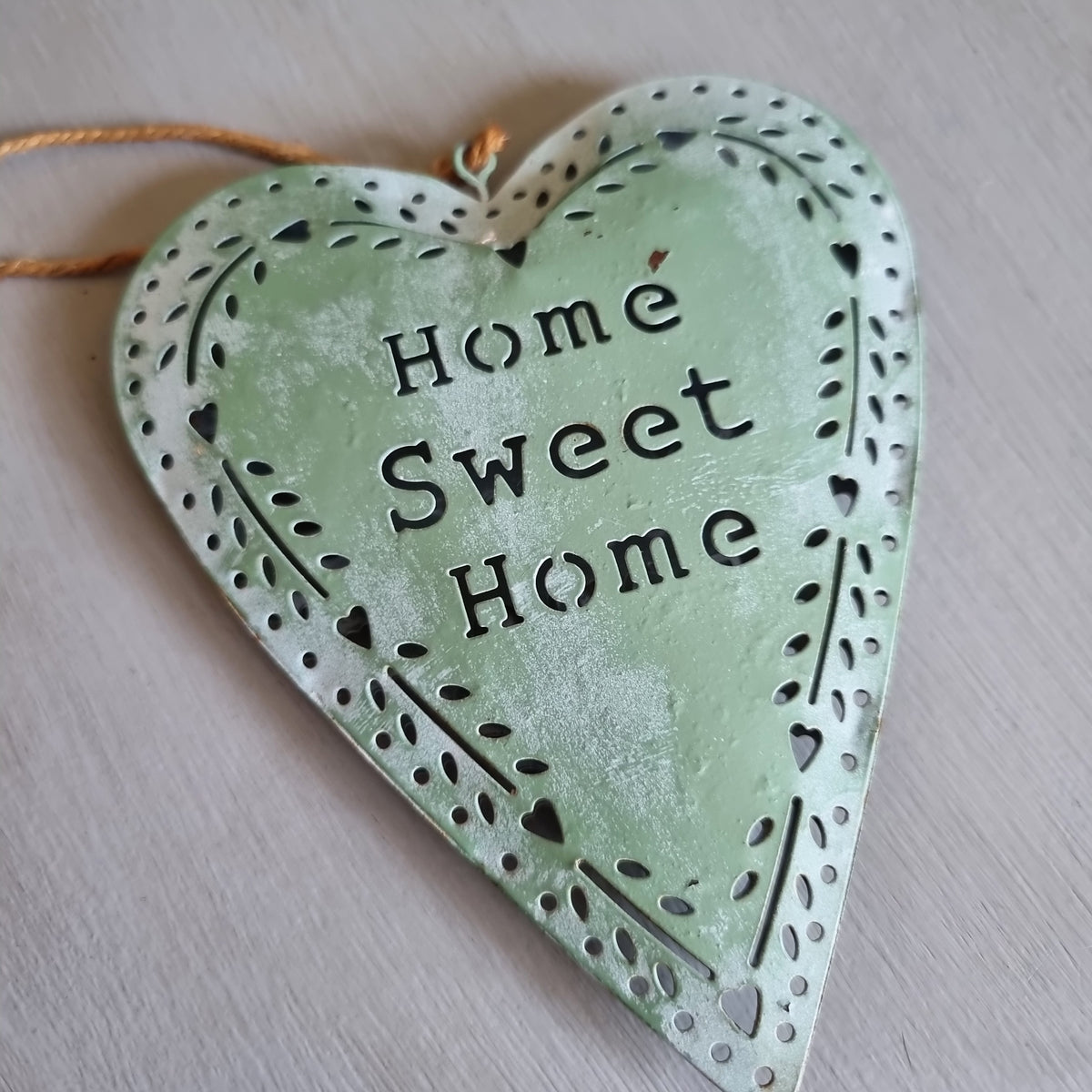 Sage green metal heart with Home Sweet Home cut out in the centre and a punched heart and leaf border, hanging from twine