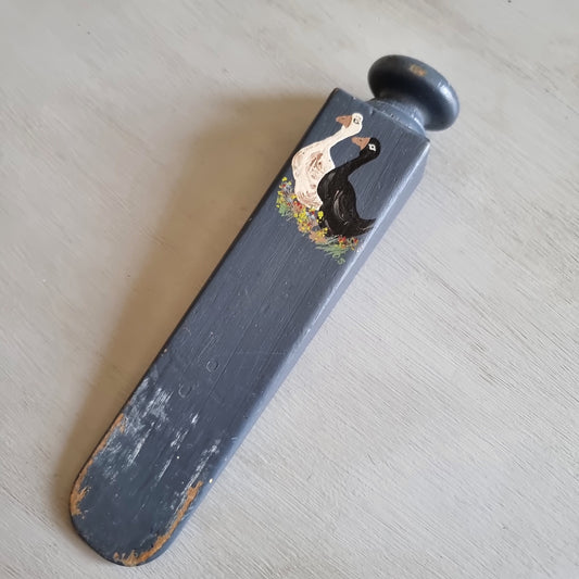 Grey painted wooden wedge door stop with a round knob, hand painted with a white goose and a black goose among flowers