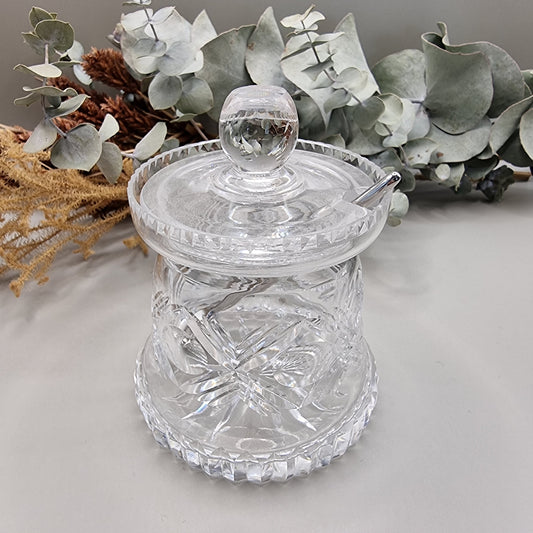 Cut glass sugar or jam jar with lid and spoon, featuring starburst pattern and faceted edge.