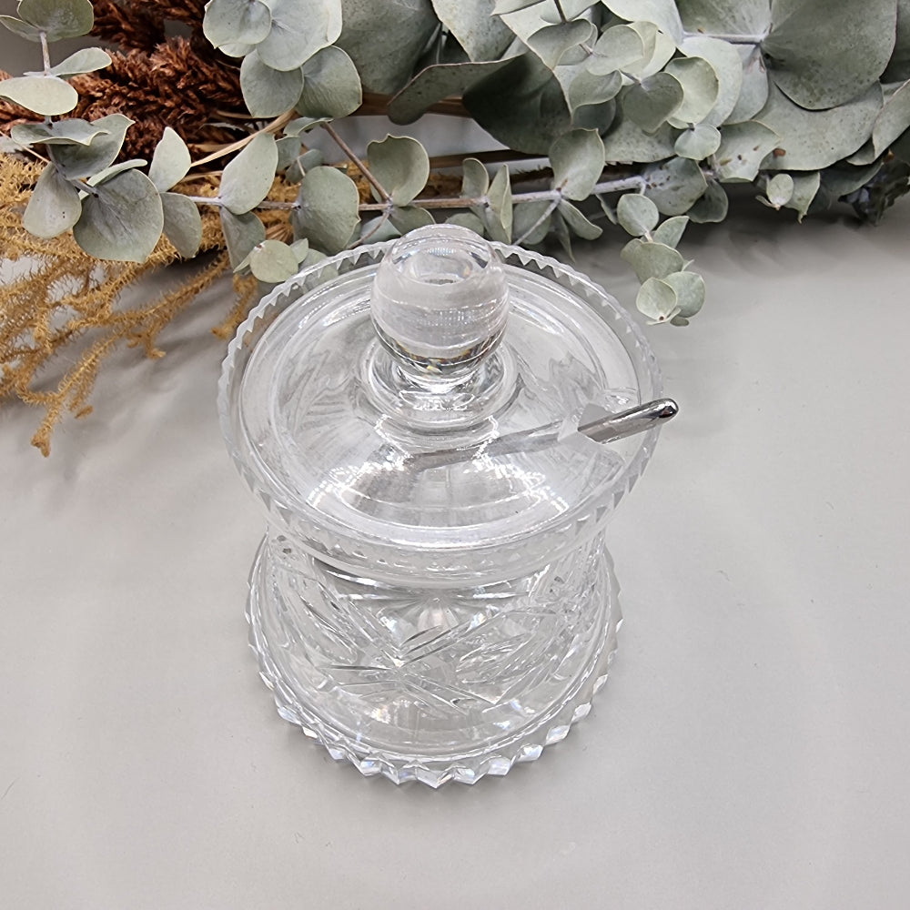 Cut glass sugar or jam jar with lid and spoon, featuring starburst pattern and faceted edge.