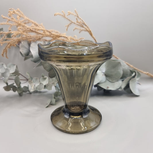 Smoky grey pedestal glass vase with fluted shape and wavy rim.
