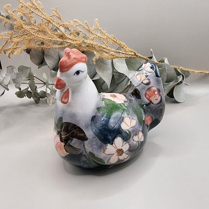 Vintage hand-painted ceramic hen figurine with soft pink and white floral design on grey and navy glaze, terracotta red comb and wattle