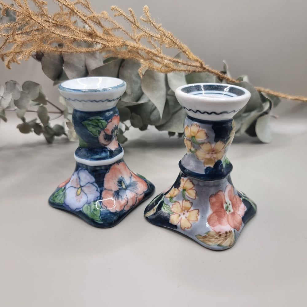 Pair of vintage hand-painted ceramic candlestick holders with pink peach and yellow floral design on navy blue glaze