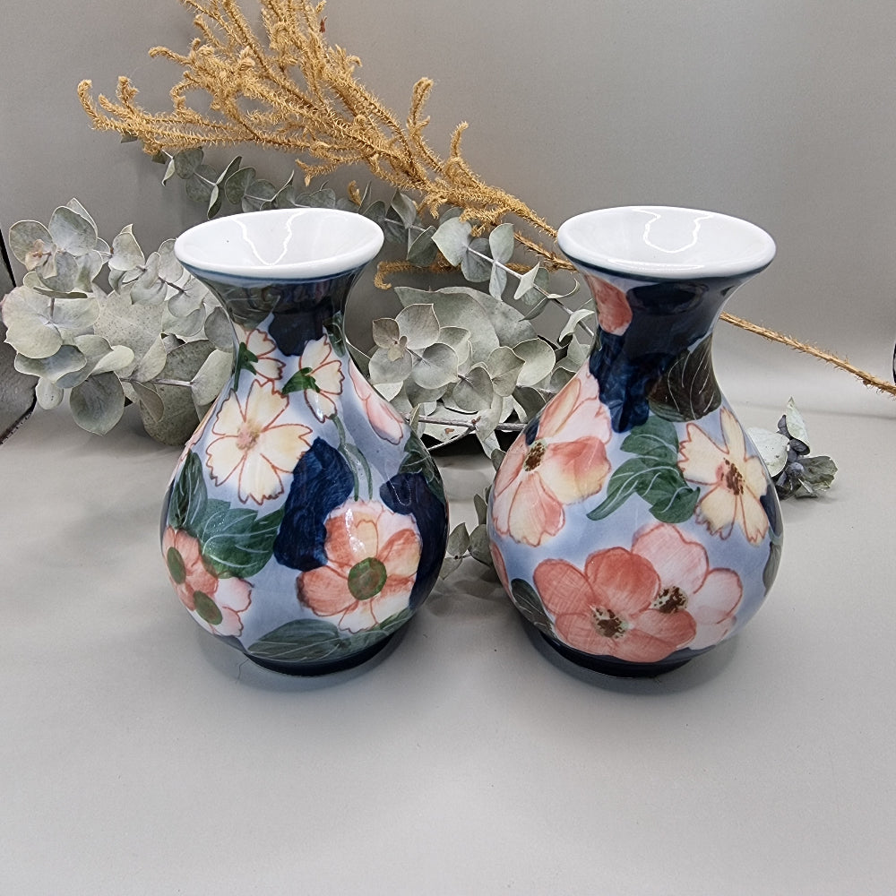 Pair of vintage hand-painted ceramic bud vases with large pink and peach floral design on periwinkle and navy blue glaze, wide flared white rim