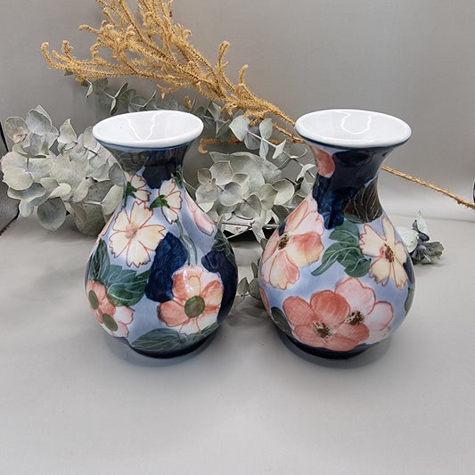 Pair of vintage hand-painted ceramic bud vases with large pink and peach floral design on periwinkle and navy blue glaze, wide flared white rim