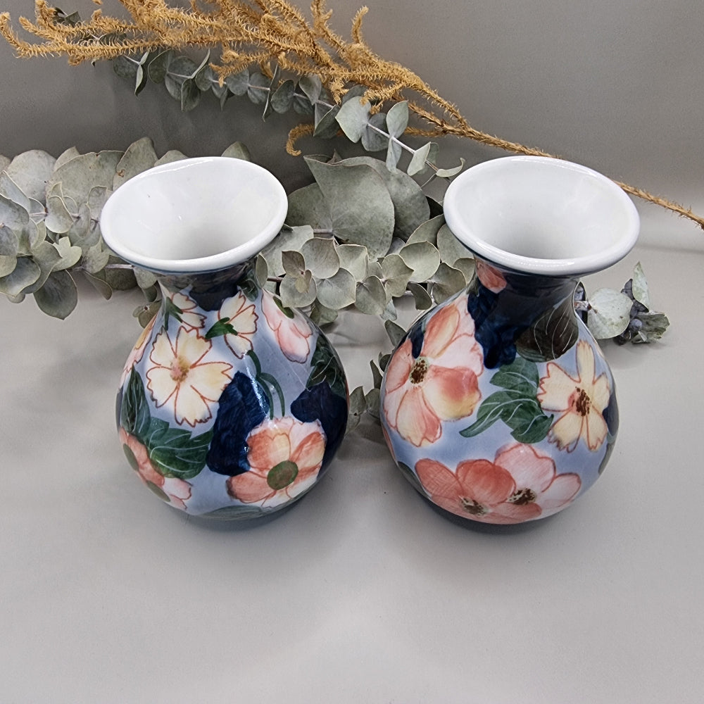Pair of vintage hand-painted ceramic bud vases with large pink and peach floral design on periwinkle and navy blue glaze, wide flared white rim