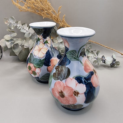 Pair of vintage hand-painted ceramic bud vases with large pink and peach floral design on periwinkle and navy blue glaze, wide flared white rim