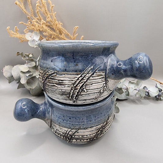 Two rustic blue soup bowls with handles and textured banding.