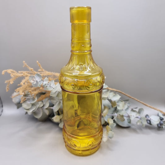 Vintage yellow glass bottle with embossed pattern and tall, sculptural shape.