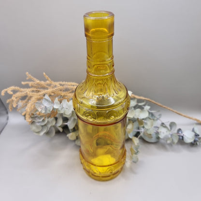Vintage yellow glass bottle with embossed pattern and tall, sculptural shape.