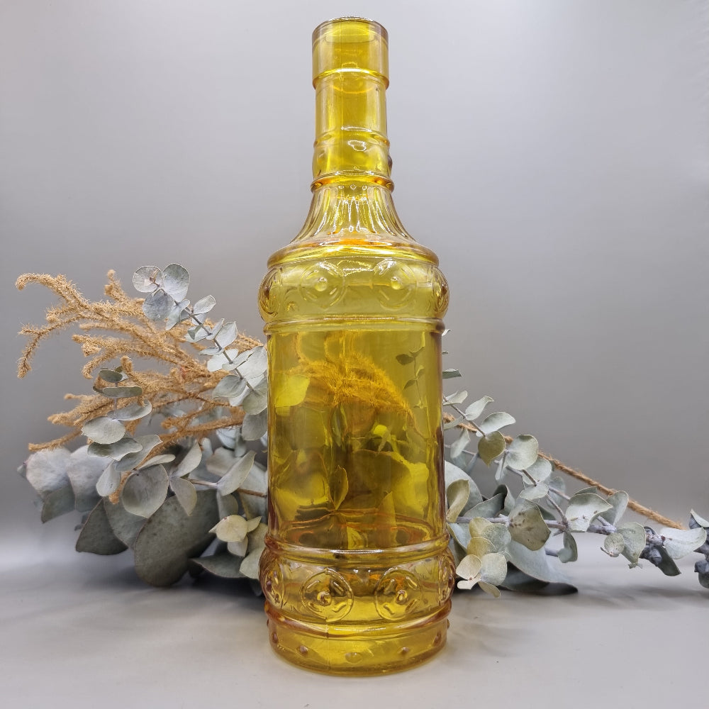 Vintage yellow glass bottle with embossed pattern and tall, sculptural shape.