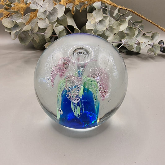 Glass paperweight with pink, blue and green floral swirl and bubble details inside.