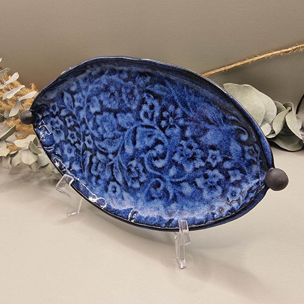Deep blue ceramic dish with embossed floral pattern and round end handles.