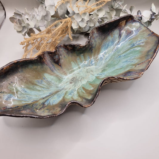 Handmade ceramic bowl with flowing form, sea-toned glaze, and textured outer surface.