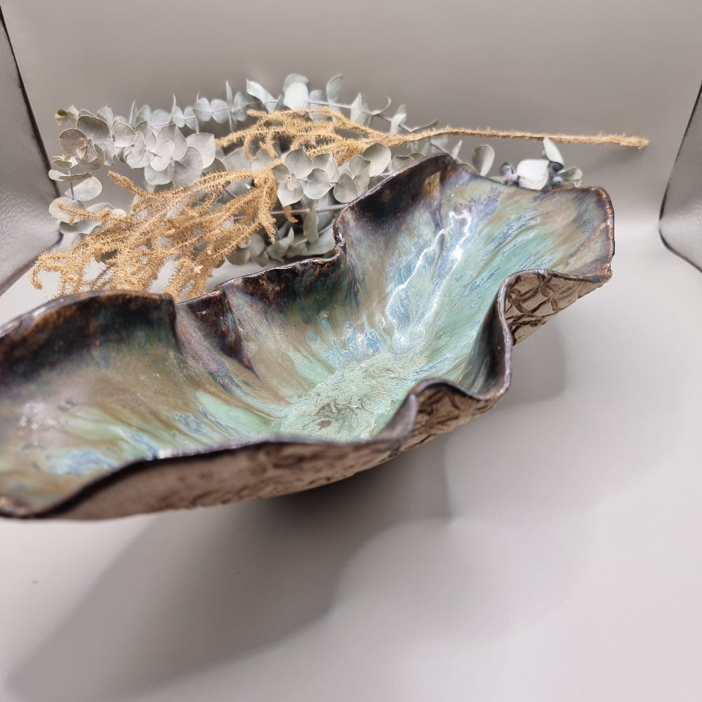 Handmade ceramic bowl with flowing form, sea-toned glaze, and textured outer surface.