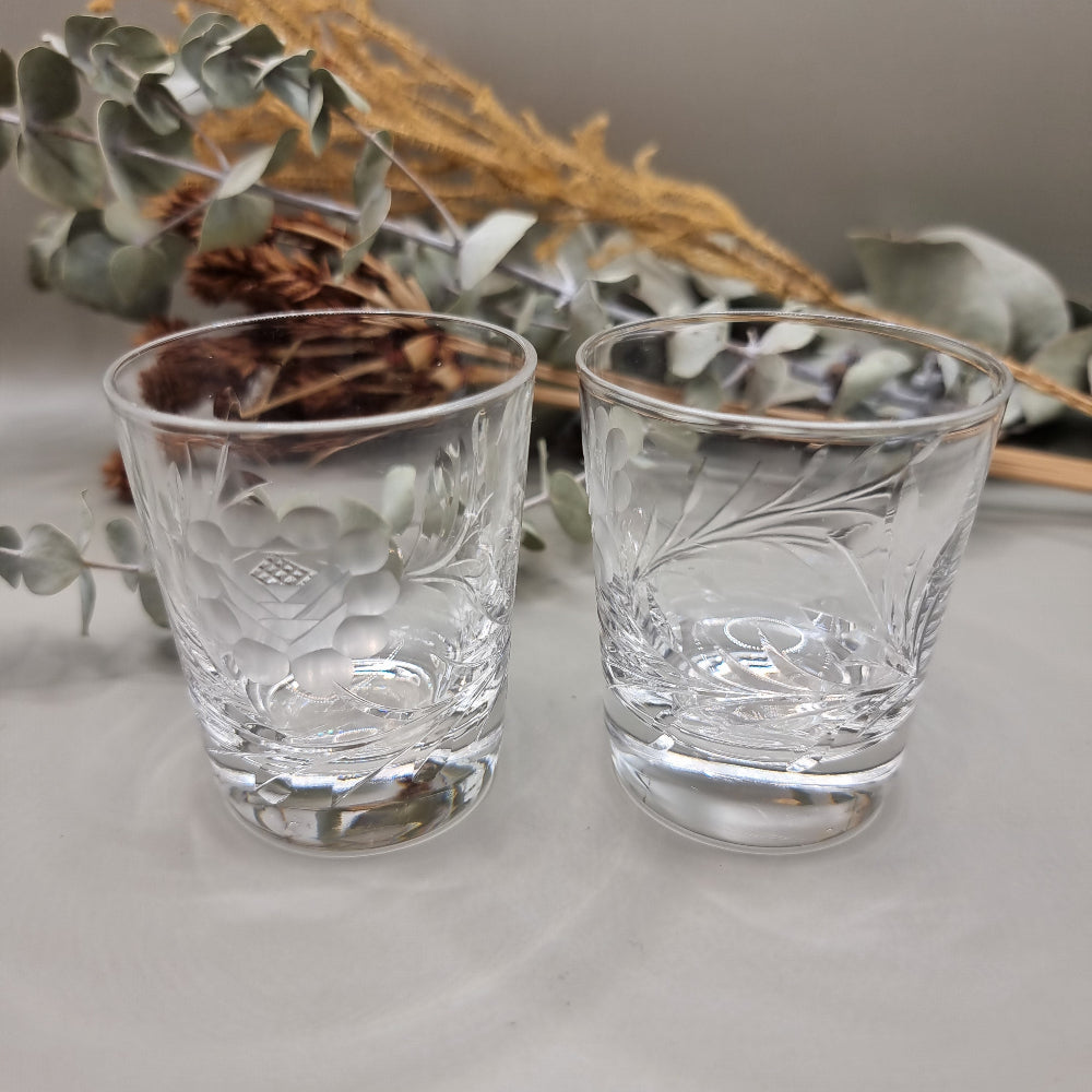 Pair of cut crystal shot glasses with etched floral and leaf pattern.