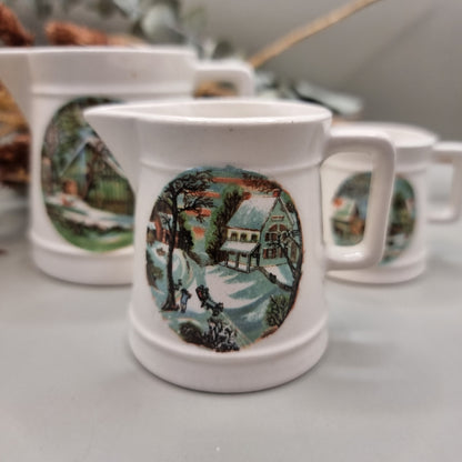 Three white ceramic measuring jugs with colourful winter countryside scenes.