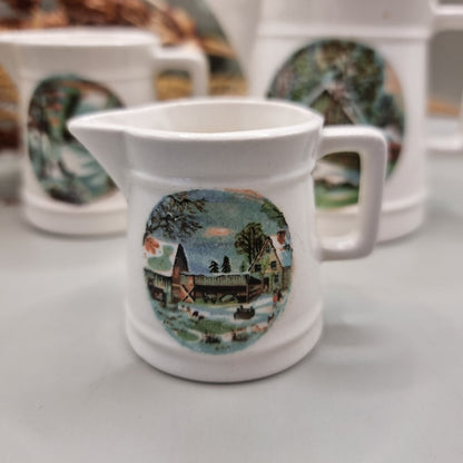 Three white ceramic measuring jugs with colourful winter countryside scenes.