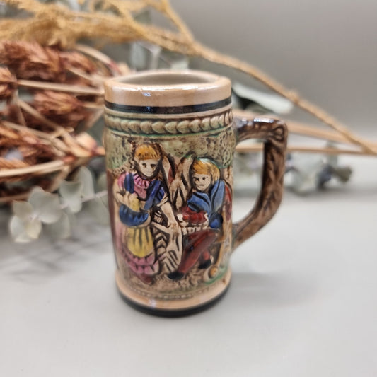 Miniature ceramic stein with embossed pastoral scene and castle design, hand-painted in earthy tones.