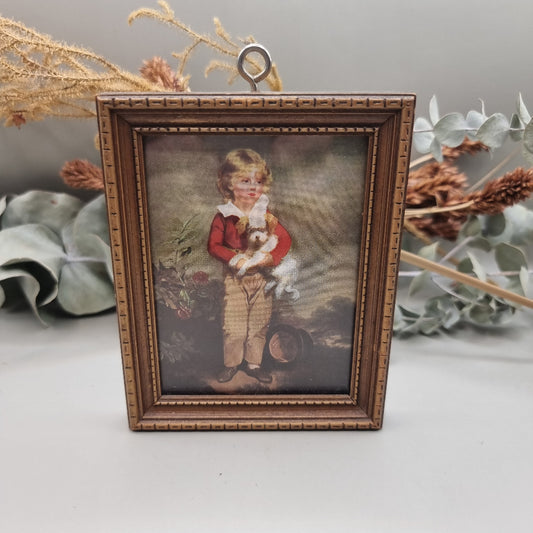 Framed vintage print of young boy in red coat holding a small white dog.