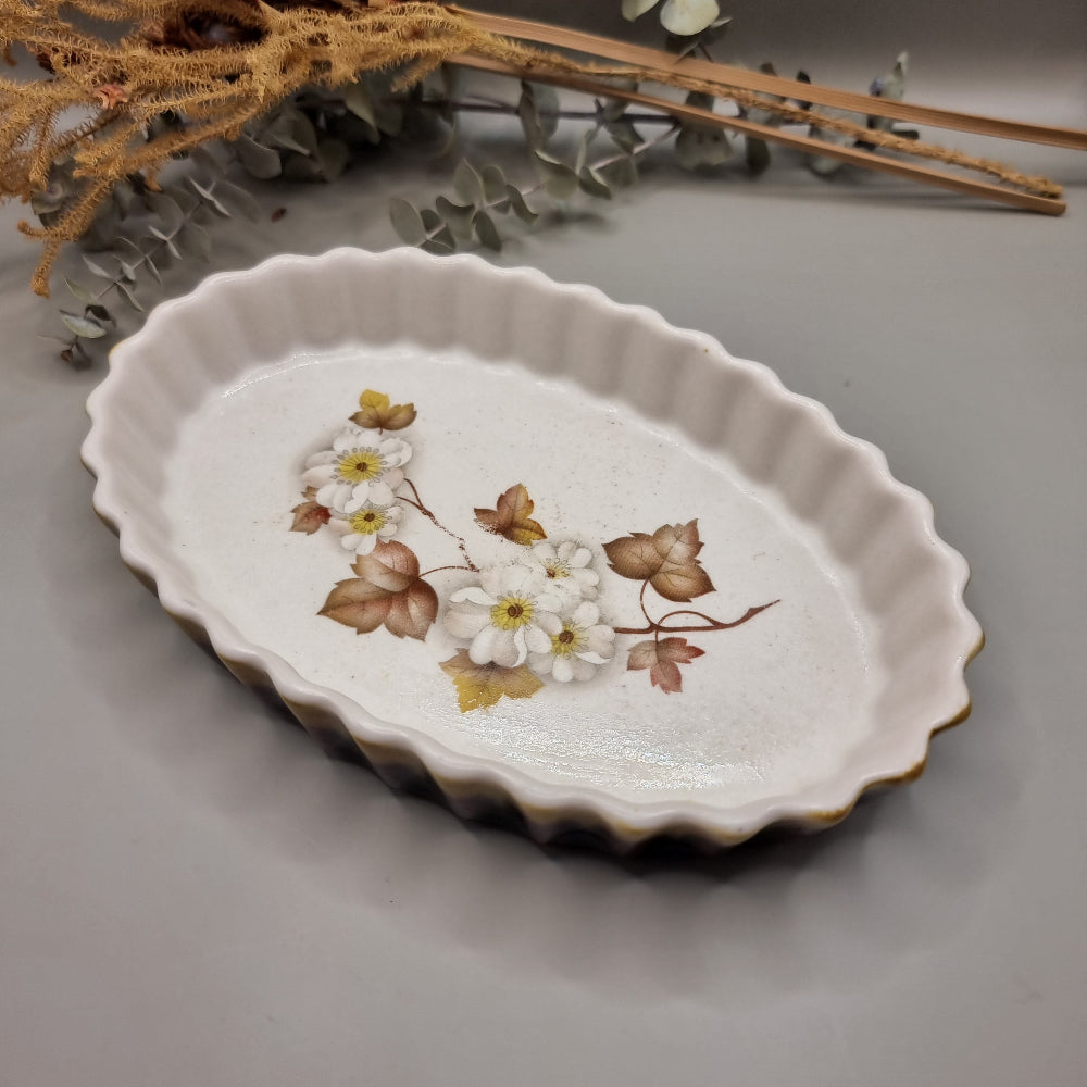 Oval ceramic tart dish with white blossom and brown leaf design, scalloped edge and rustic glaze.