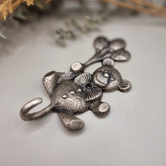 Silver-tone teddy bear wall hook holding balloons with a curved tail hook for hanging items.