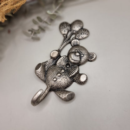 Silver-tone teddy bear wall hook holding balloons with a curved tail hook for hanging items.