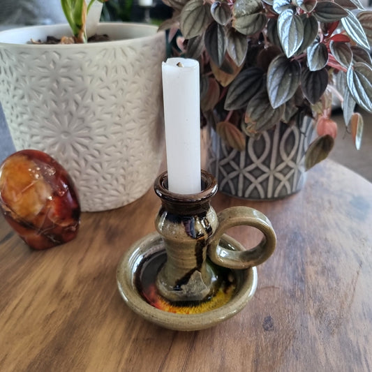Handmade ceramic chamberstick with earthy glaze and finger loop, holding a white taper candle