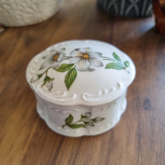 Vintage porcelain trinket box with scalloped edges and floral design featuring white flowers and green leaves