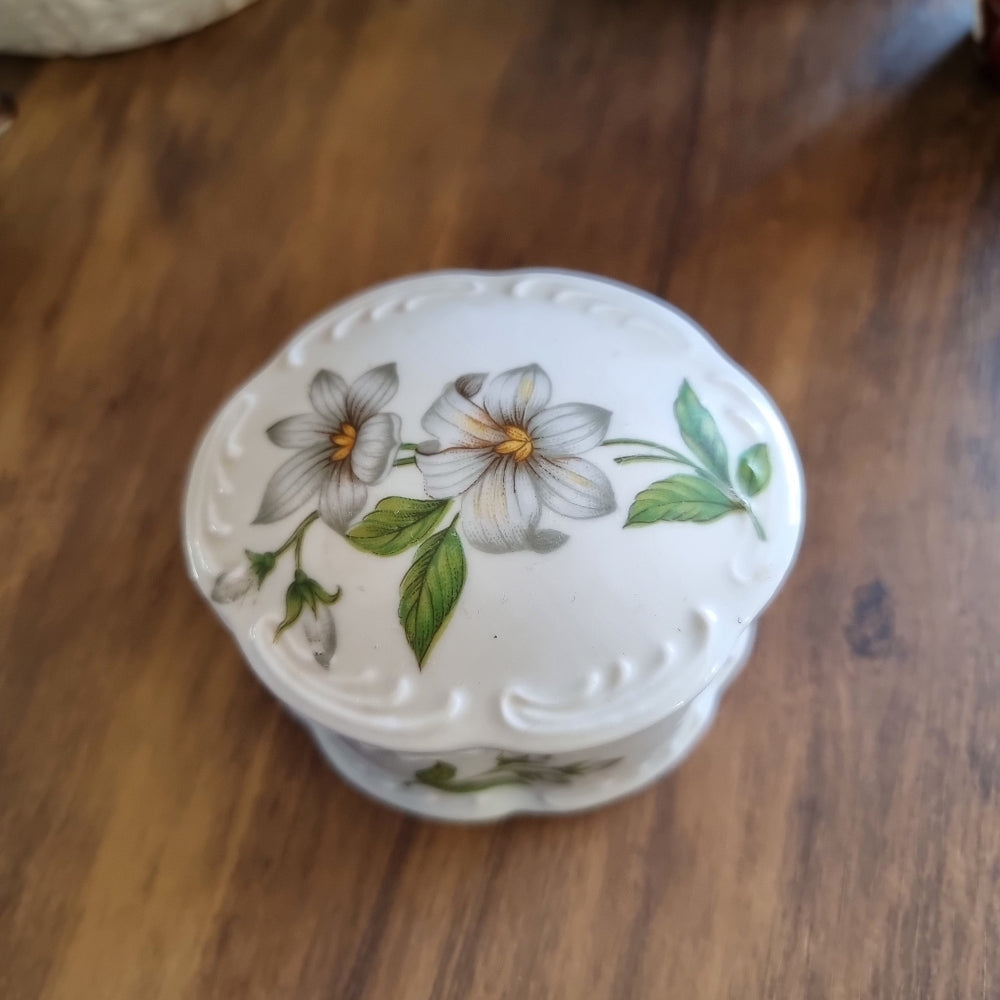 Vintage porcelain trinket box with scalloped edges and floral design featuring white flowers and green leaves