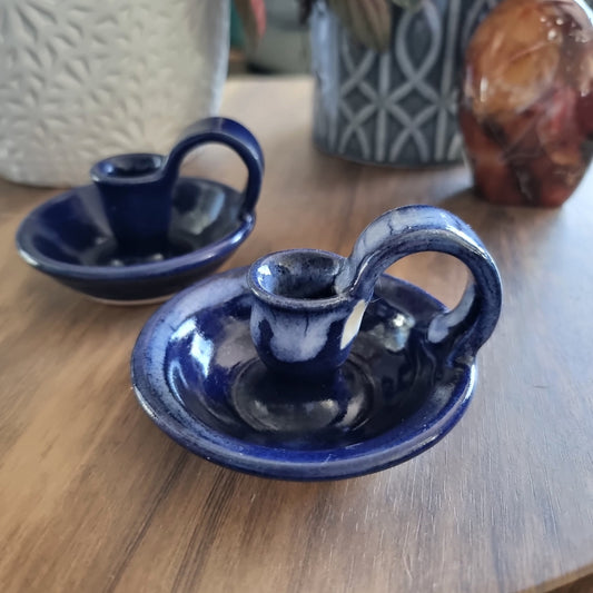 Pair of cobalt blue ceramic chamberstick candle holders with finger loops on a wooden table