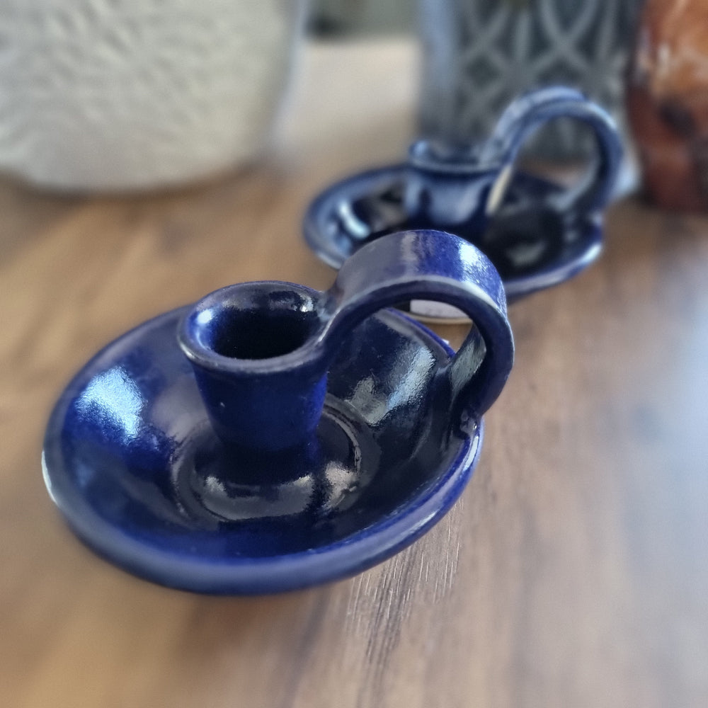 Pair of cobalt blue ceramic chamberstick candle holders with finger loops on a wooden table