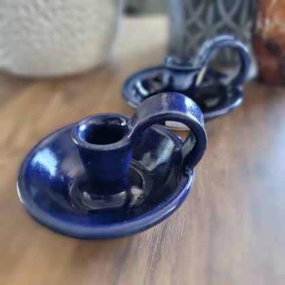 Pair of cobalt blue ceramic chamberstick candle holders with finger loops on a wooden table