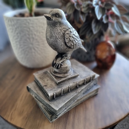 Rustic bird figurine perched on a stack of vintage-style books with a weathered stone finish