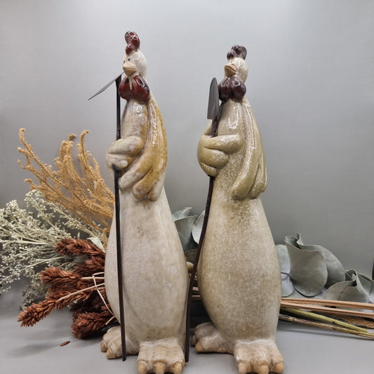 Tall ceramic rooster sculptures holding garden tools, rustic and whimsical style.