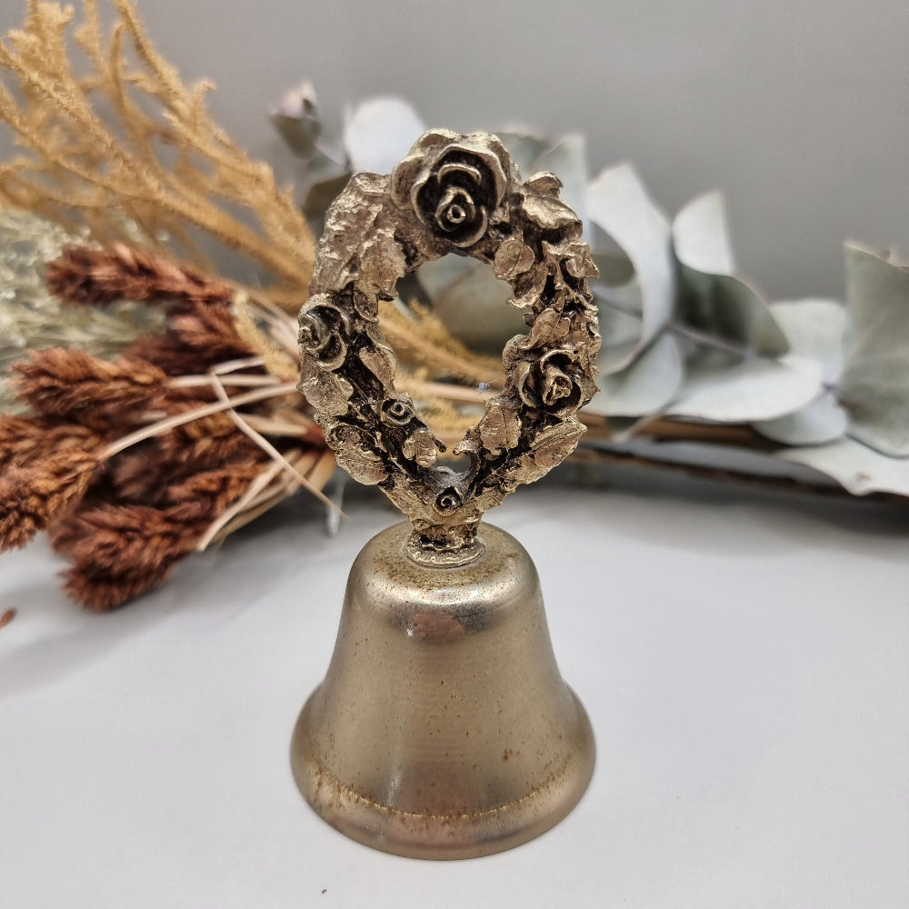 Vintage brass bell with rose wreath handle and aged patina.