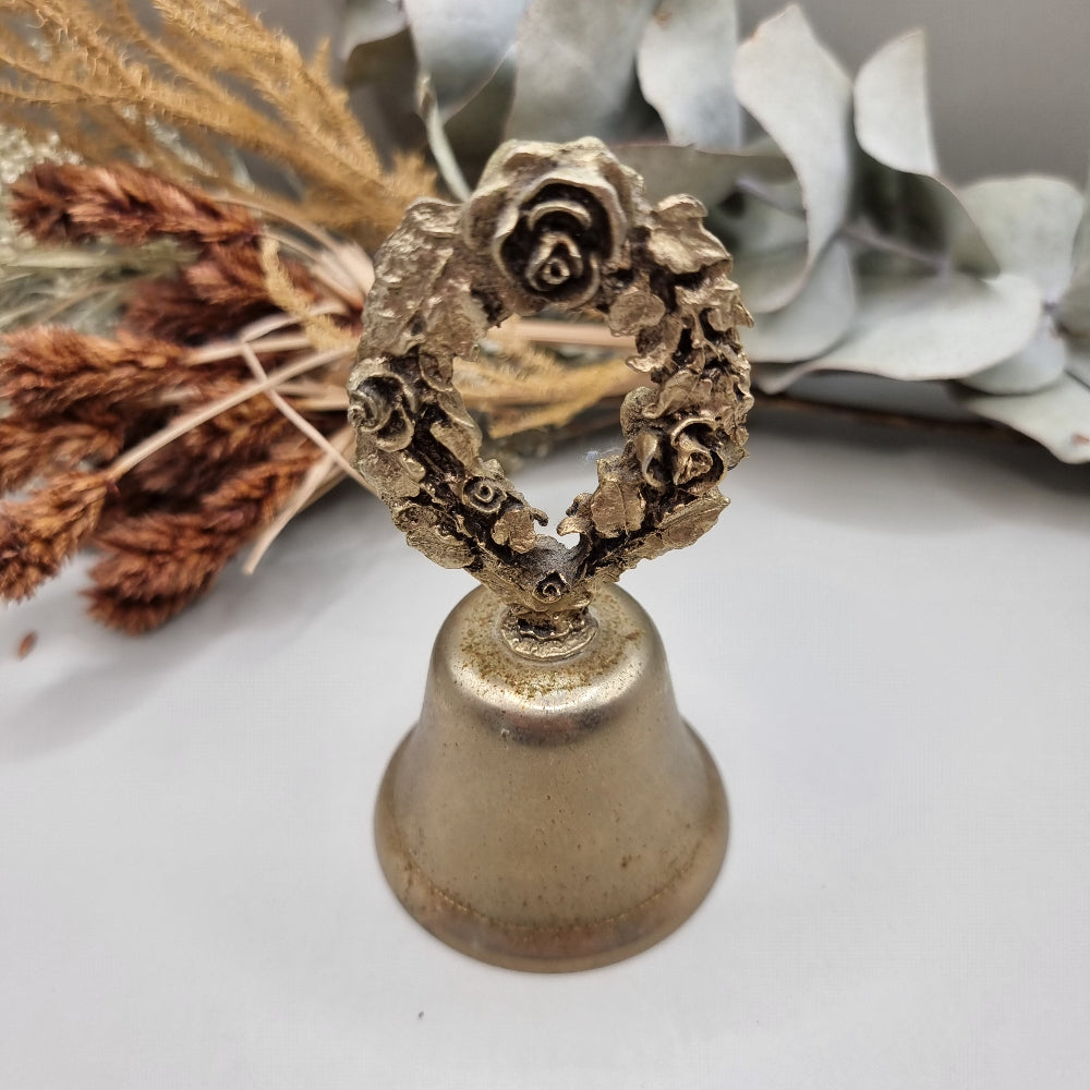 Vintage brass bell with rose wreath handle and aged patina.