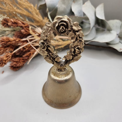 Vintage brass bell with rose wreath handle and aged patina.