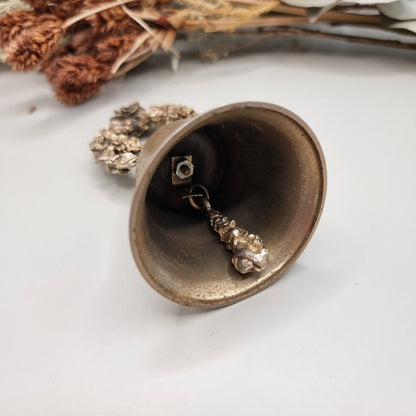 Vintage brass bell with rose wreath handle and aged patina.