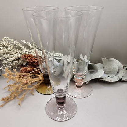 Set of three champagne flutes with pink, amber, and plum coloured bases