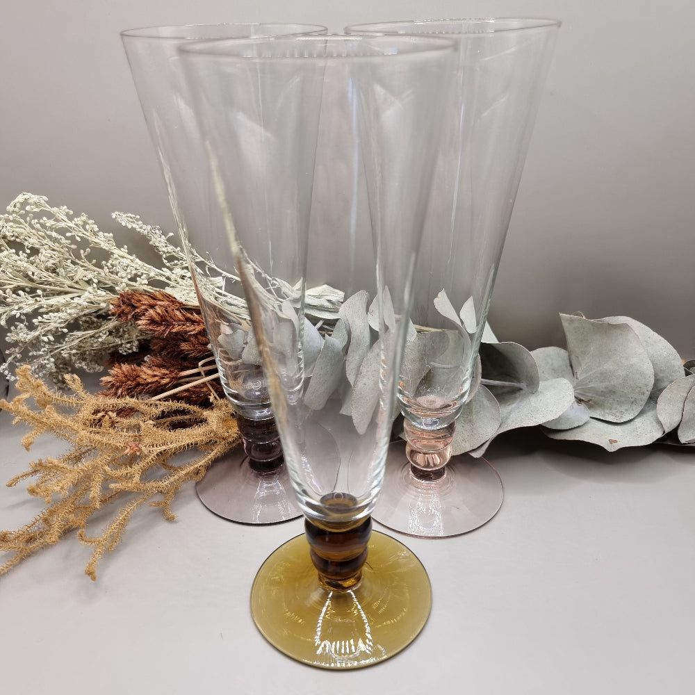 Set of three champagne flutes with pink, amber, and plum coloured bases