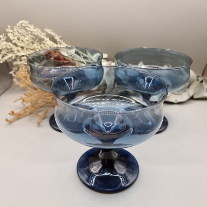 Set of three smoky blue glass dessert coupes with short stems and rounded bowls.
