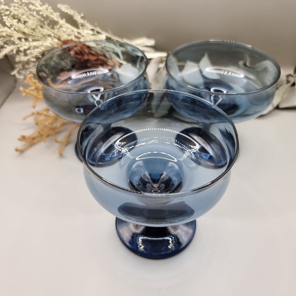 Set of three smoky blue glass dessert coupes with short stems and rounded bowls.